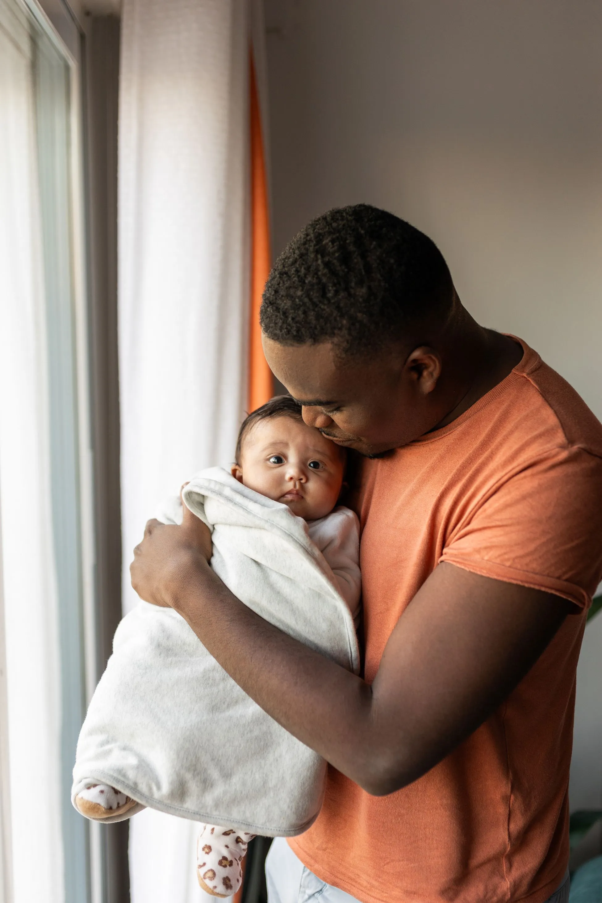 father holding baby next to window